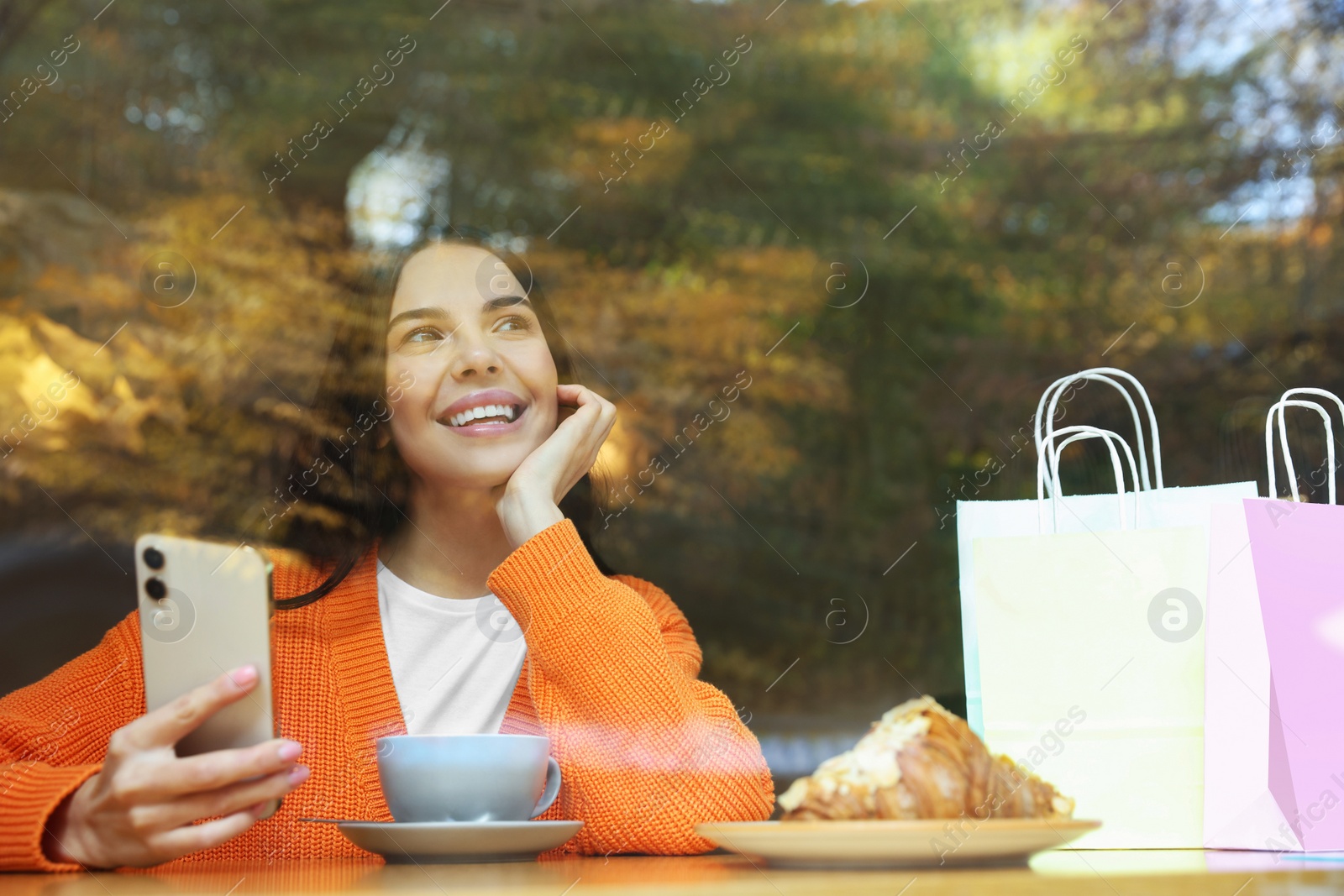 Photo of Special Promotion. Happy young woman using smartphone in cafe, view from outdoors