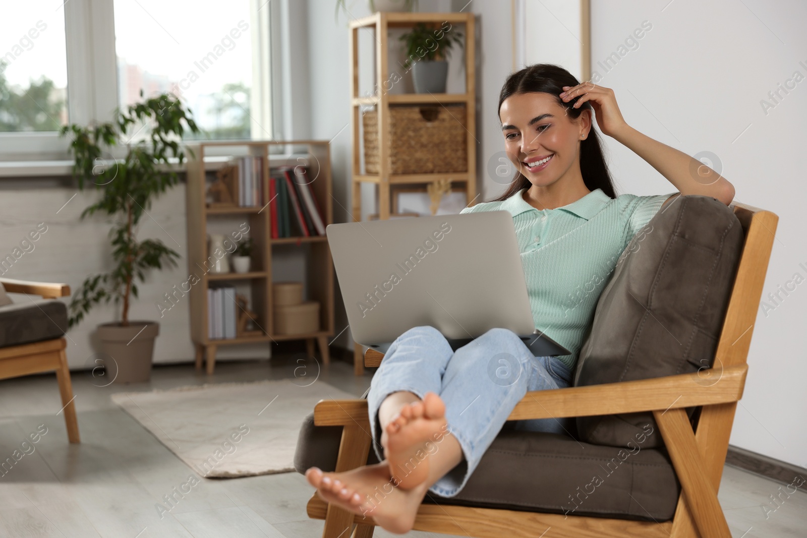 Photo of Young woman working with laptop in armchair at home