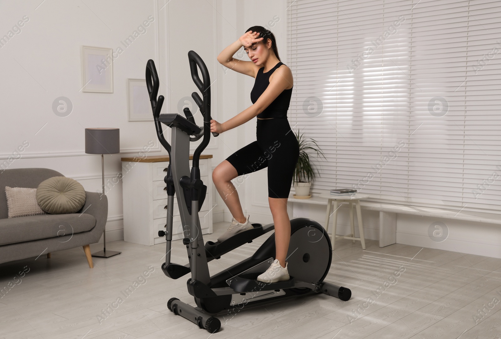 Photo of Young woman feeling tired of training on 	
elliptical machine at home