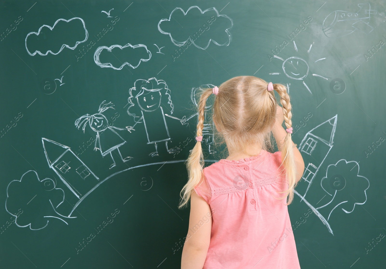 Photo of Little child drawing family with white chalk on blackboard