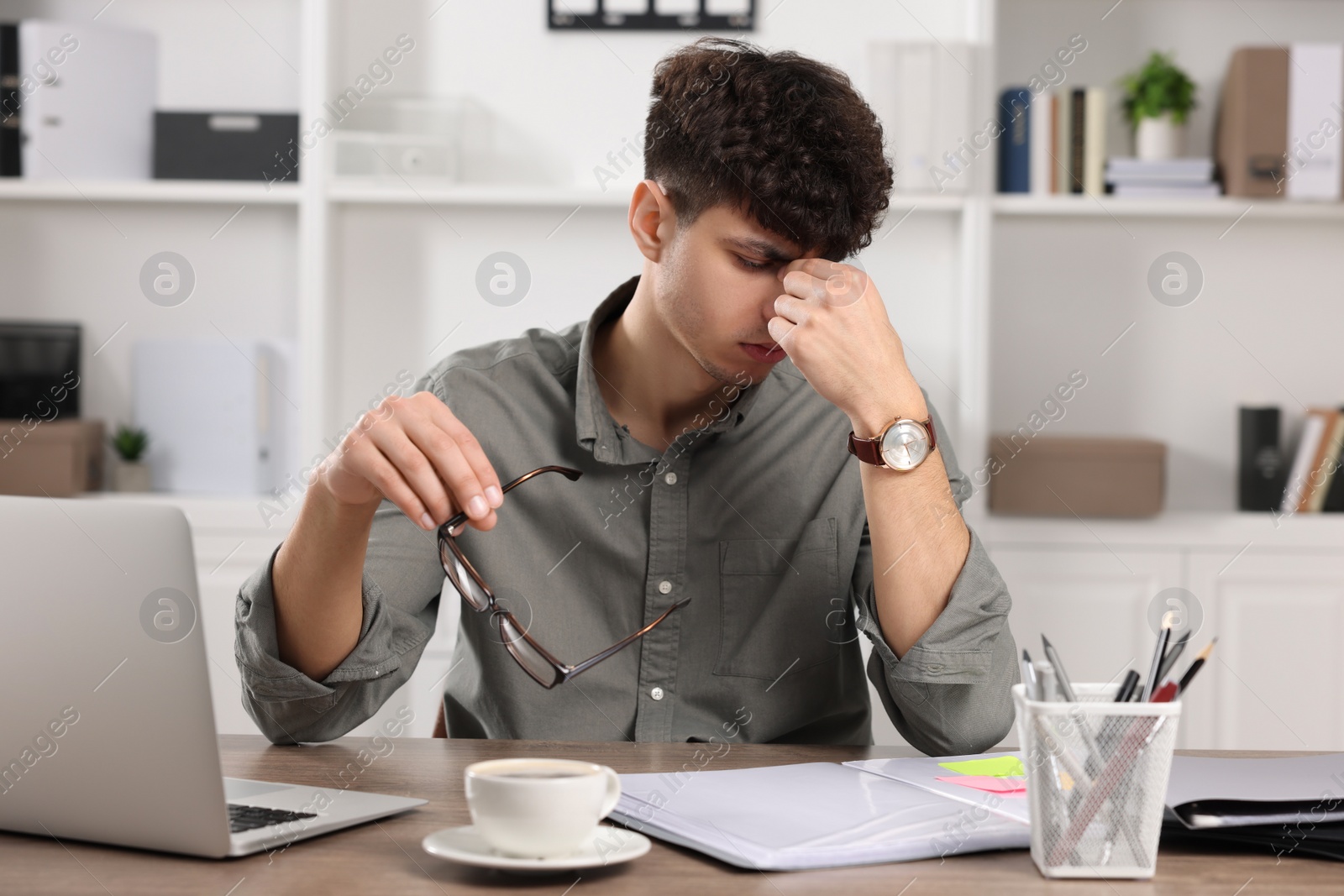 Photo of Tired young man working at table in office. Deadline concept