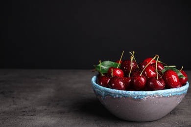 Photo of Bowl with delicious sweet cherries on grey table. Space for text