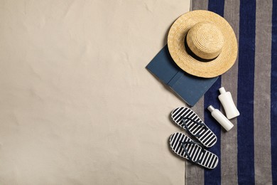 Beach towel, hat, book, sun protection products and flip flops on sand, flat lay. Space for text