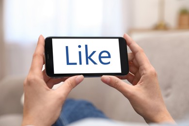 Woman holding smartphone with word Like on screen indoors, closeup