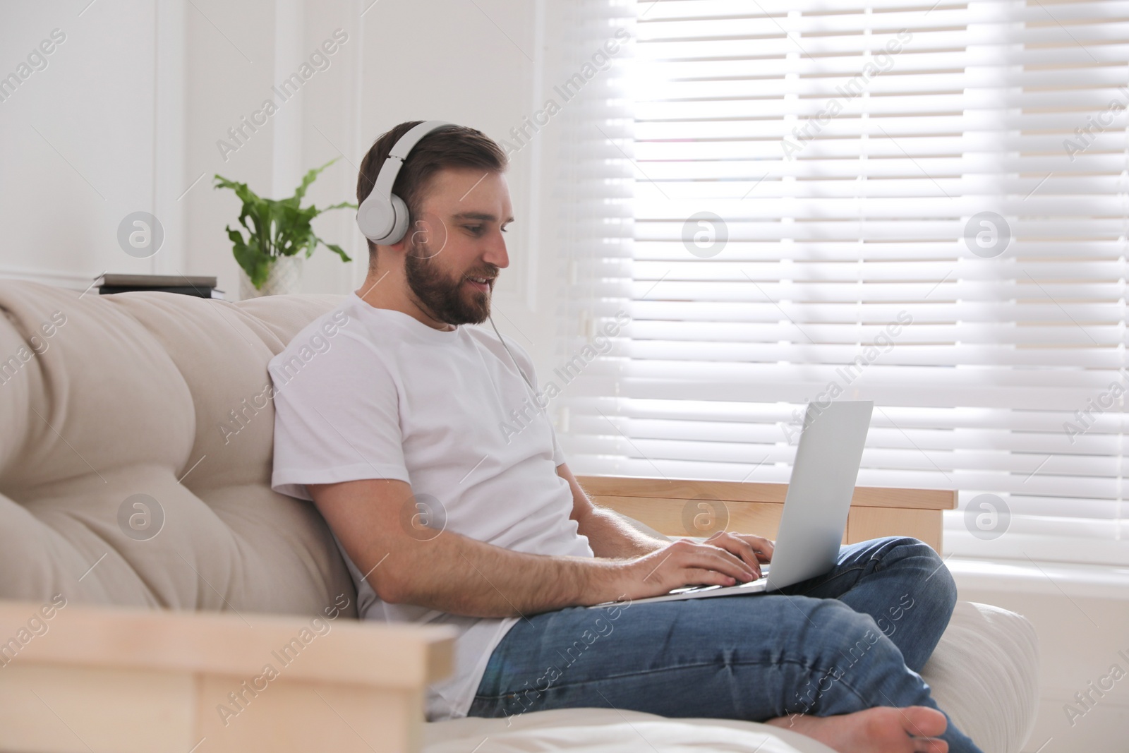 Photo of Man with laptop and headphones sitting on sofa at home