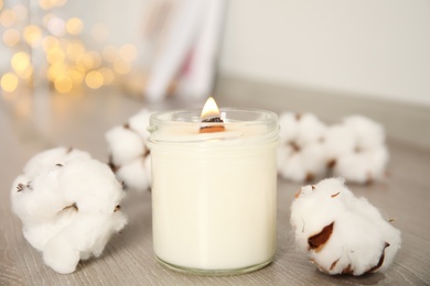 Burning candle and cotton flowers on wooden table