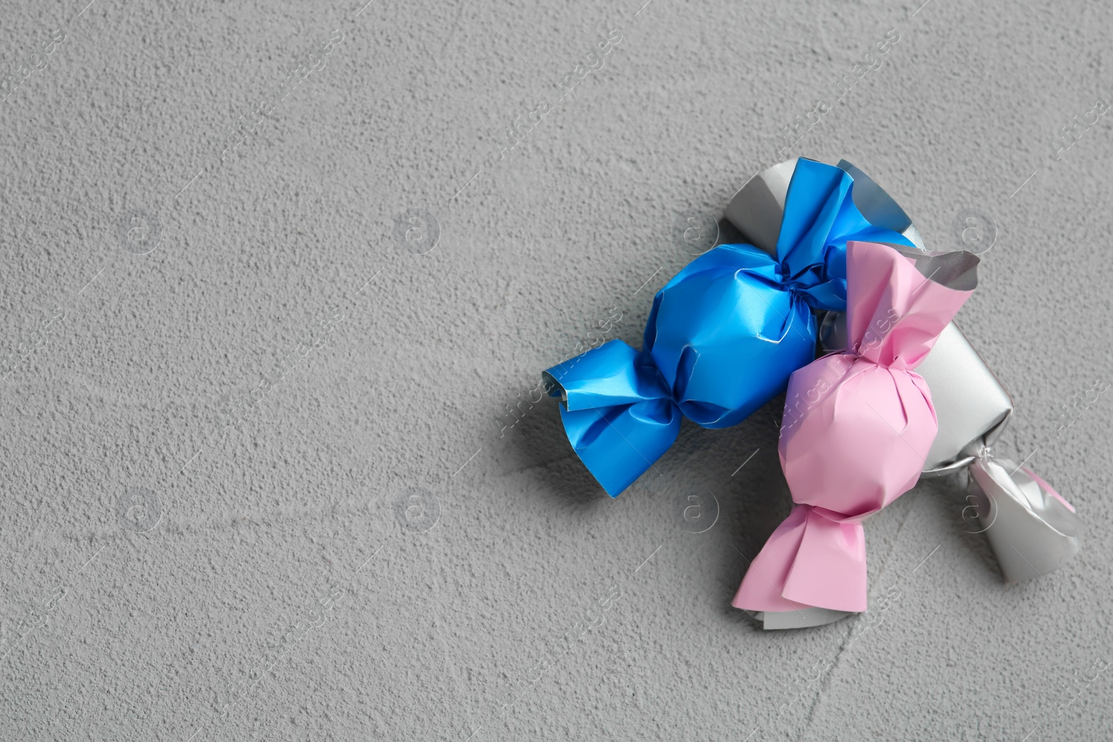 Photo of Candies in colorful wrappers on grey table, flat lay. Space for text