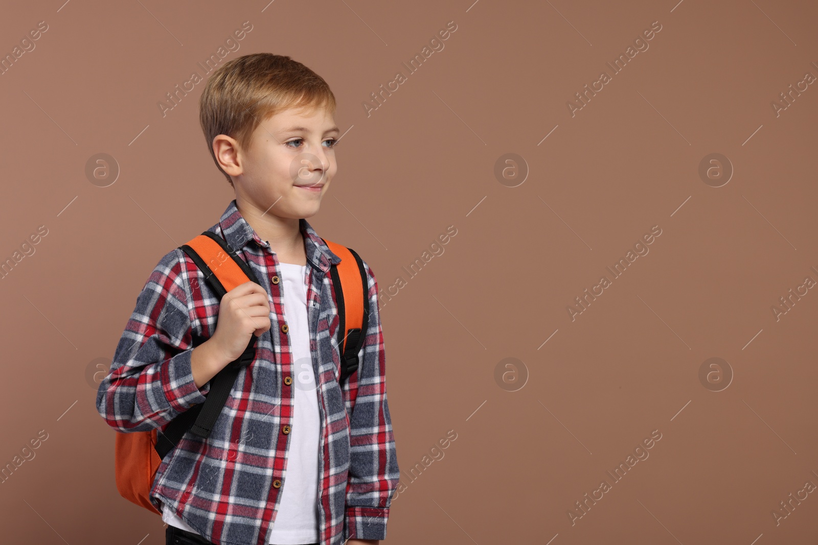 Photo of Happy schoolboy with backpack on brown background, space for text