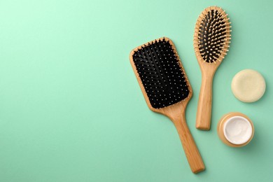 Wooden hairbrushes and different cosmetic products on turquoise background, flat lay. Space for text