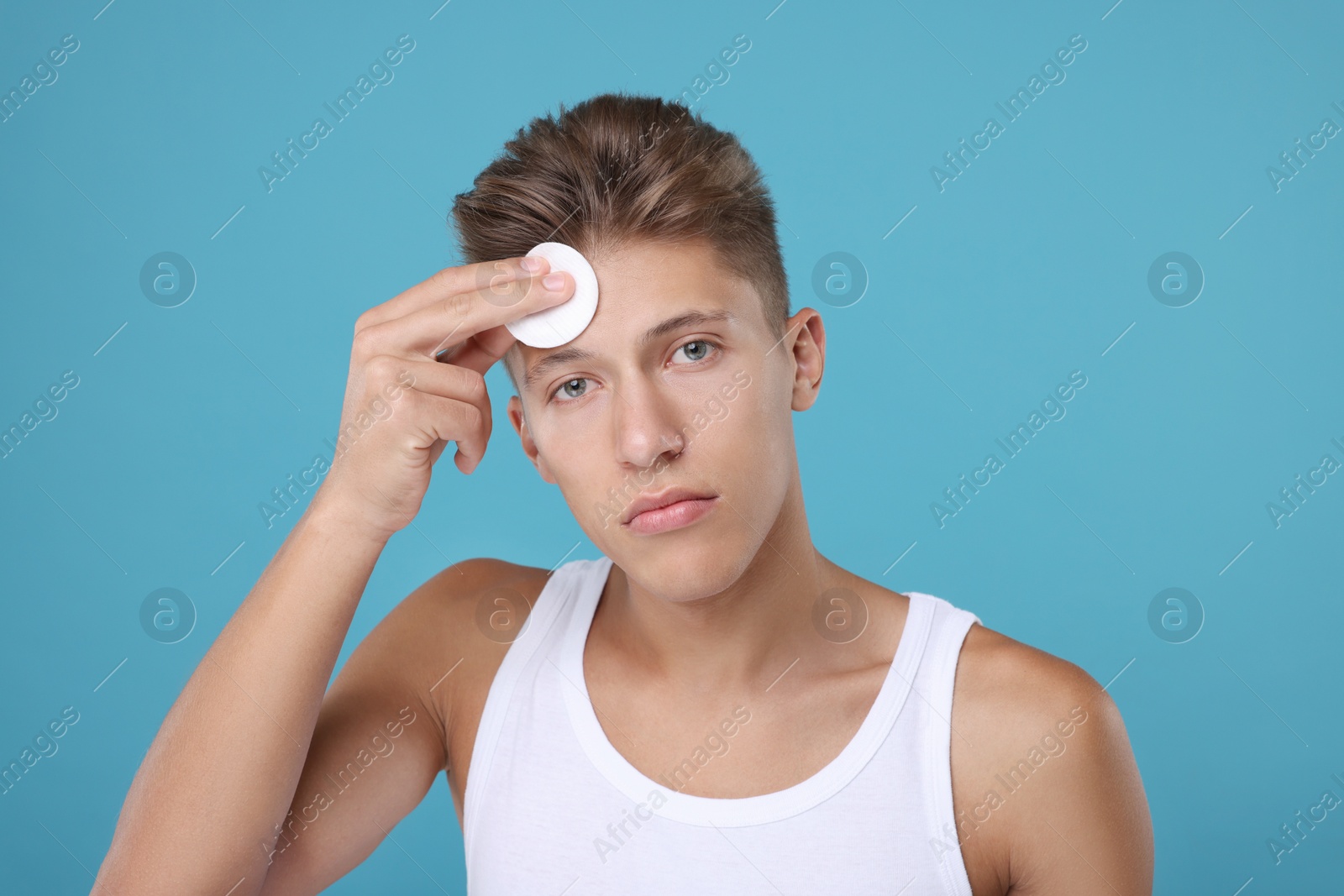 Photo of Handsome man cleaning face with cotton pad on light blue background