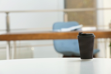 Cardboard cup of coffee on table indoors. Space for text