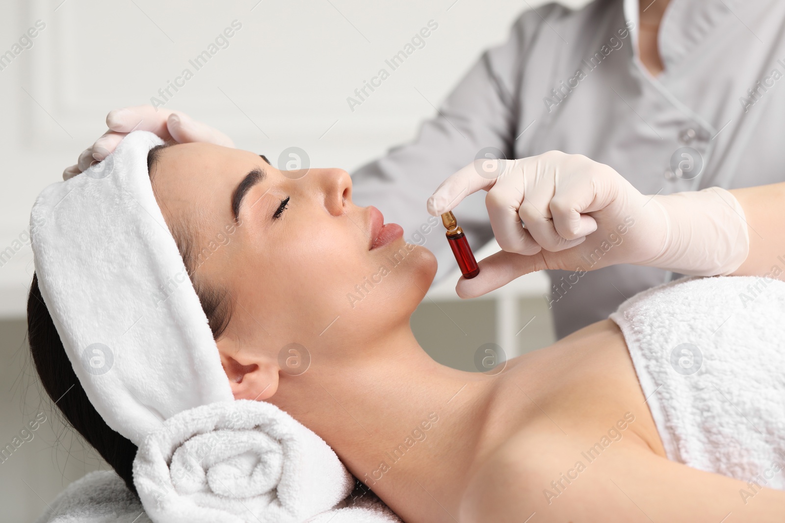 Photo of Professional cosmetologist holding skincare ampoule while working with client in clinic, closeup