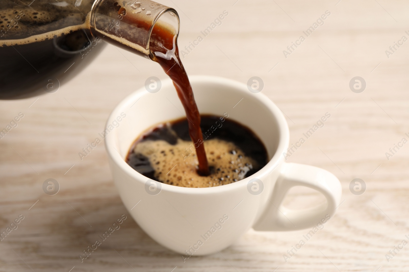 Photo of Pouring coffee into cup at light wooden table, closeup