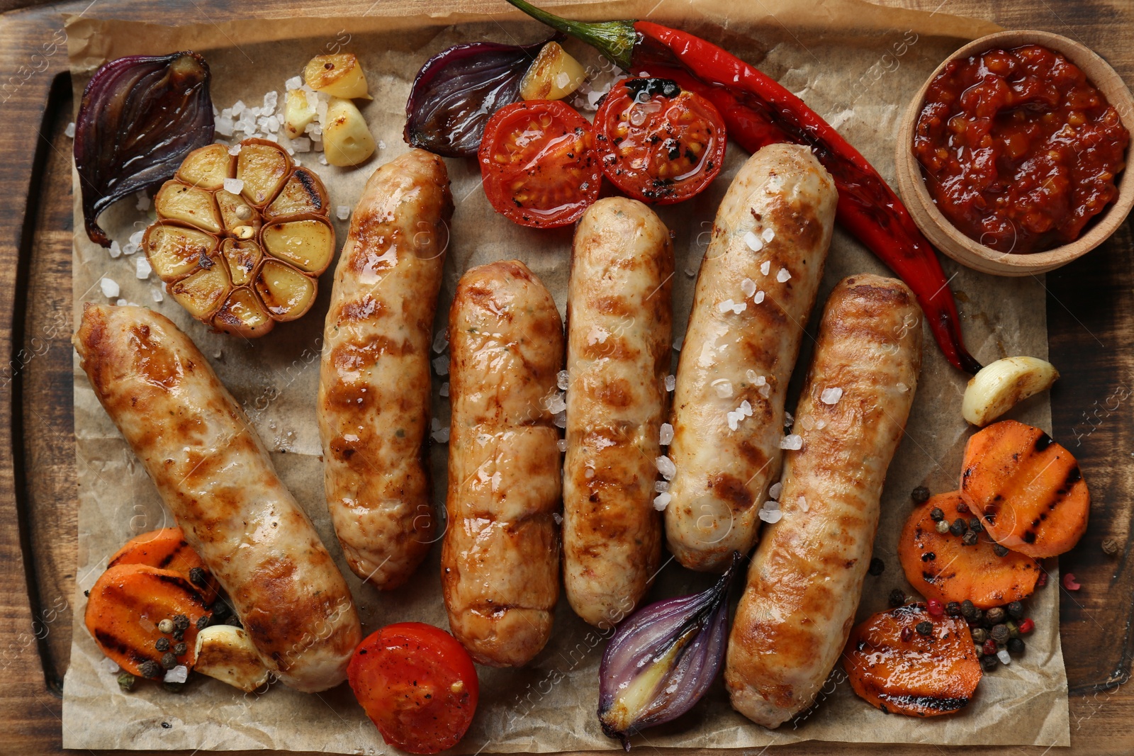 Photo of Tasty grilled sausages and products on wooden board, flat lay