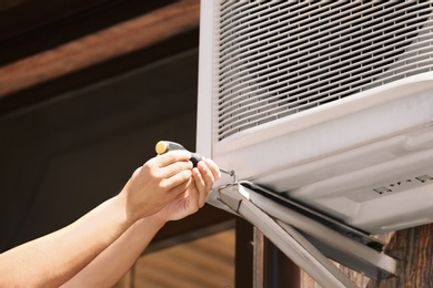 Photo of Professional technician maintaining modern air conditioner outdoors, closeup