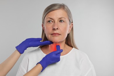 Endocrinologist examining thyroid gland of patient on light grey background, closeup