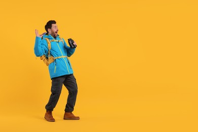Photo of Emotional man with backpack and binoculars on orange background, space for text. Active tourism