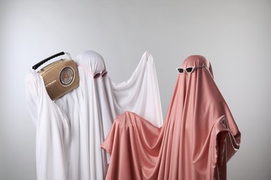 Photo of Glamorous ghosts. Women in color sheets and sunglasses with retro radio receiver on light grey background
