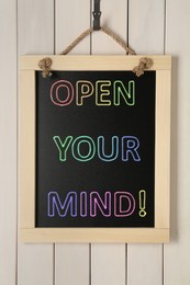Image of Small chalkboard with motivational quote Open your mind hanging on white wooden wall