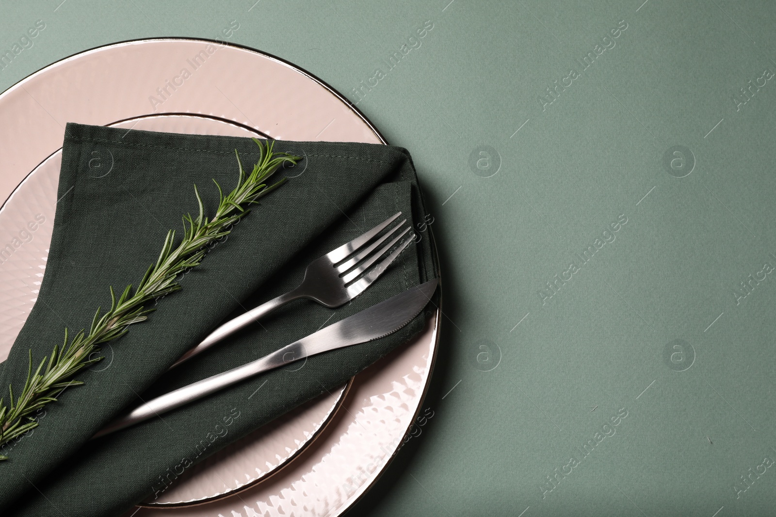 Photo of Stylish table setting. Plates, cutlery, napkin and rosemary on green background, top view with space for text