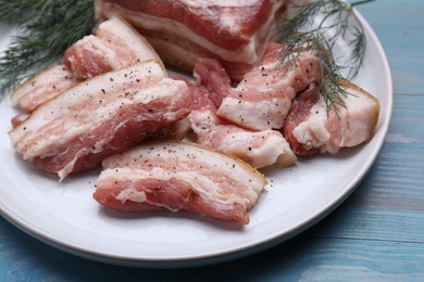 Photo of Pieces of pork fatback with dill on light blue wooden table, closeup
