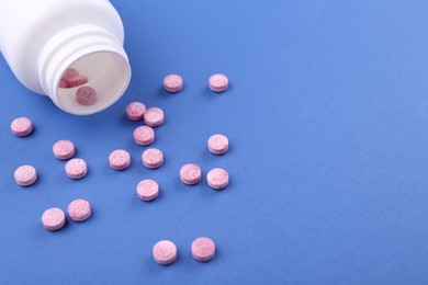 Photo of Bottle and vitamin pills on blue background, closeup. Space for text