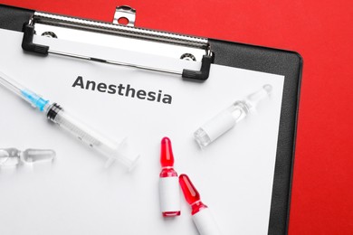 Photo of Clipboard with word Anesthesia, syringe and ampules on red background, top view