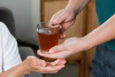 Photo of Caregiver giving tea to elderly woman at home, closeup