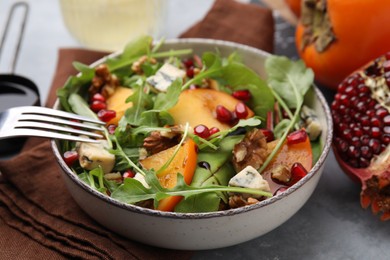 Photo of Tasty salad with persimmon, blue cheese, pomegranate and walnuts served on light grey table, closeup