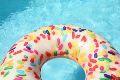 Photo of Bright inflatable doughnut ring floating in swimming pool on sunny day. Space for text