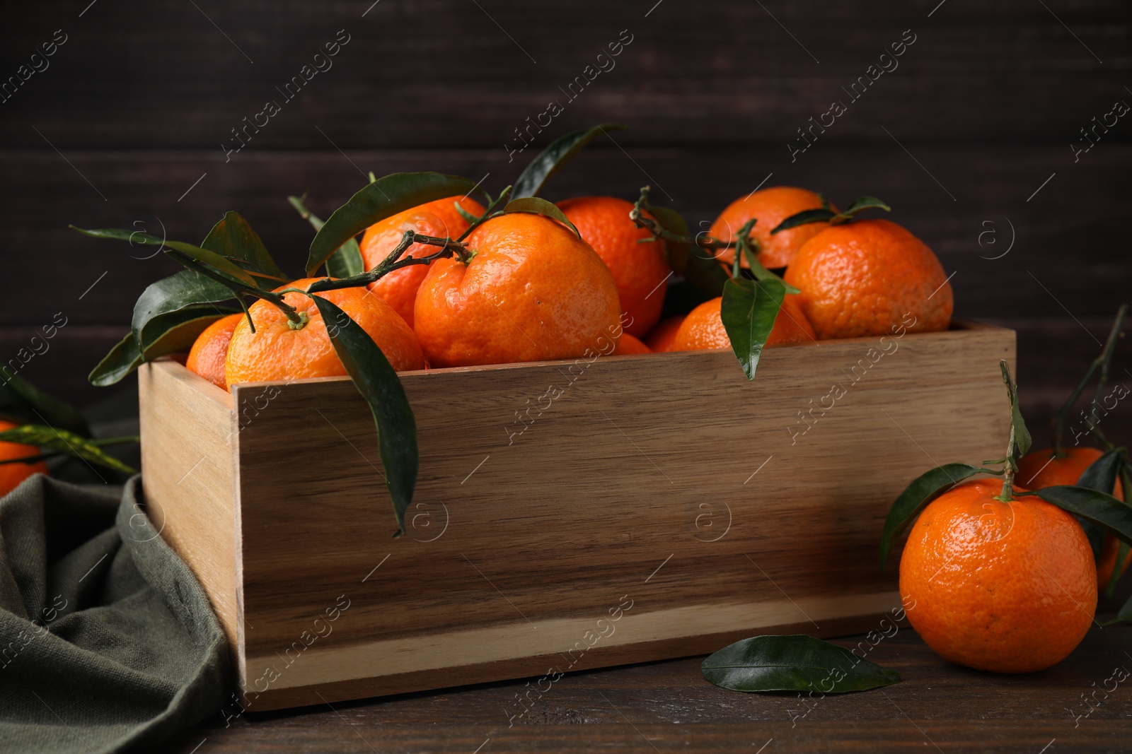Photo of Fresh ripe tangerines with green leaves in crate on wooden table