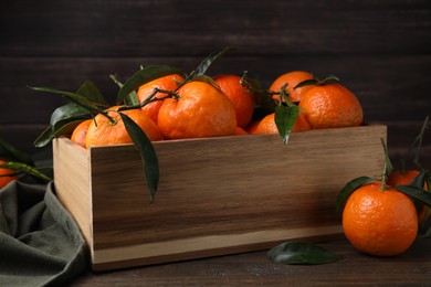 Fresh ripe tangerines with green leaves in crate on wooden table