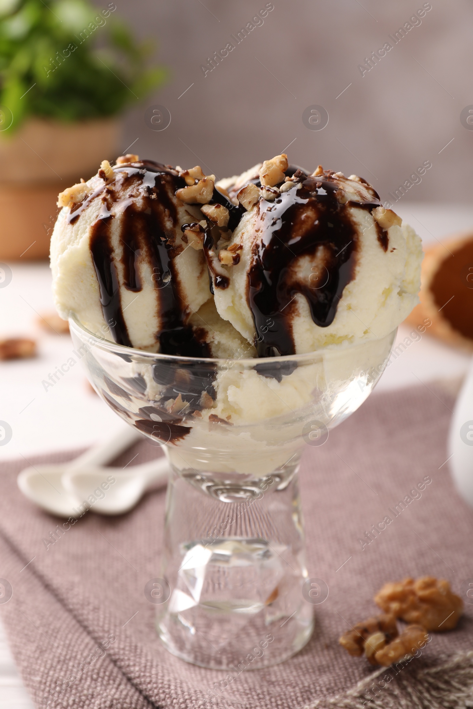 Photo of Tasty ice cream with chocolate topping and nuts in glass dessert bowl on table, closeup