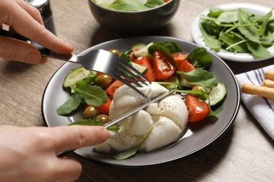 Woman eating delicious burrata salad at wooden table, closeup