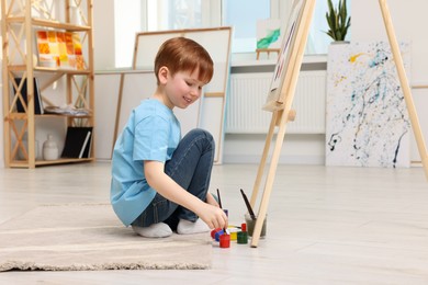 Photo of Little boy painting in studio. Using easel to hold canvas