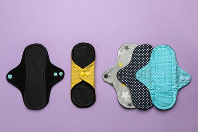 Many reusable cloth menstrual pads on violet background, flat lay