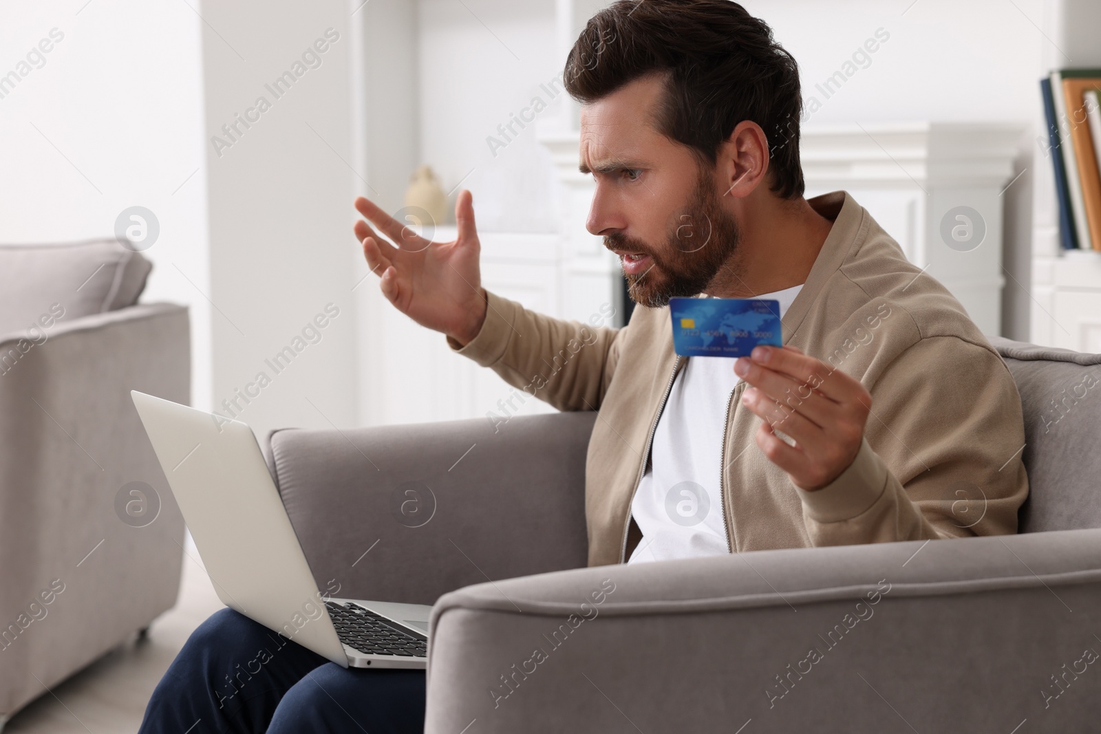 Photo of Shocked man with laptop and credit card in armchair at home. Be careful - fraud