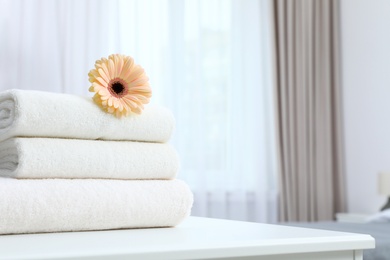 Stack of fresh towels with flower on table in bedroom. Space for text