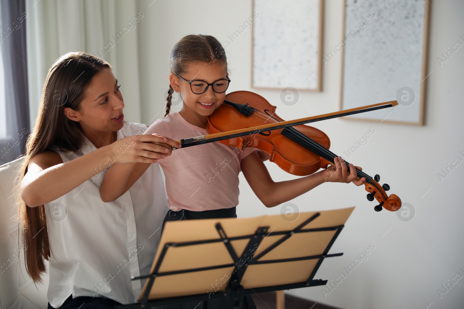 Photo of Young woman teaching little girl to play violin indoors