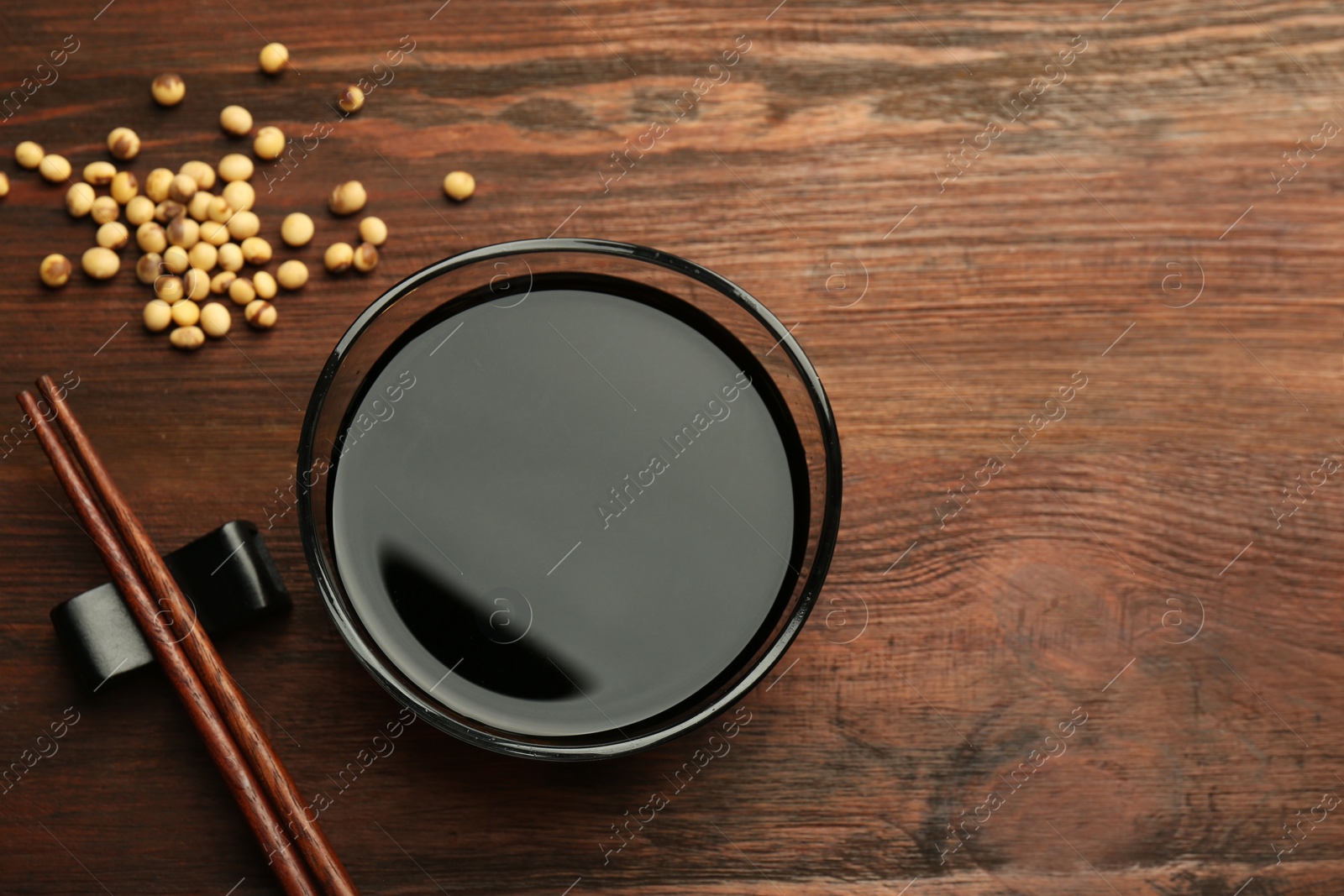 Photo of Soy sauce in bowl, soybeans and chopsticks on wooden table, flat lay. Space for text