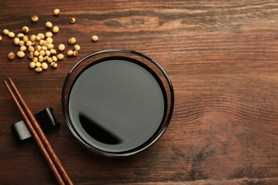 Soy sauce in bowl, soybeans and chopsticks on wooden table, flat lay. Space for text