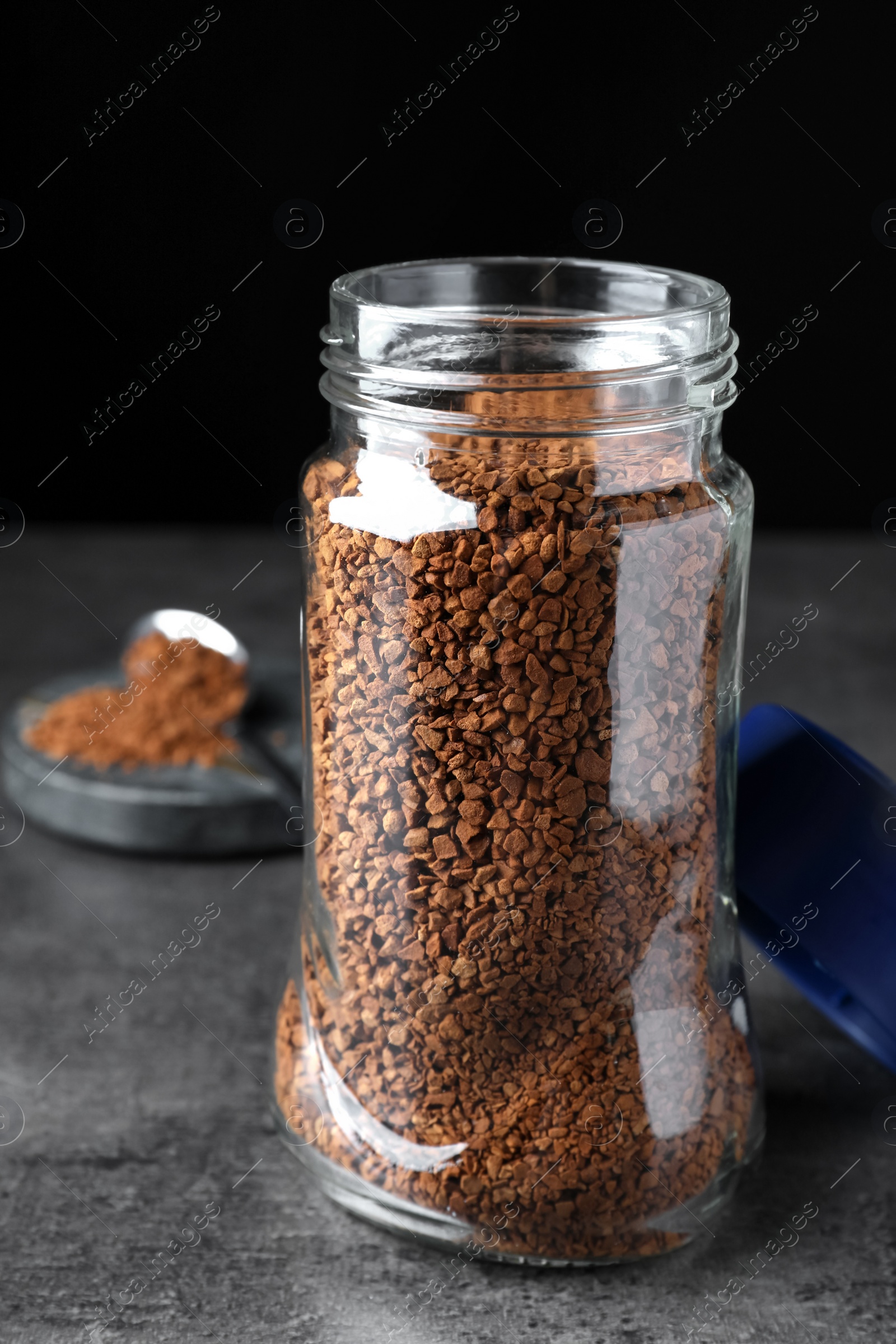 Photo of Glass jar of instant coffee on grey table against black background, closeup