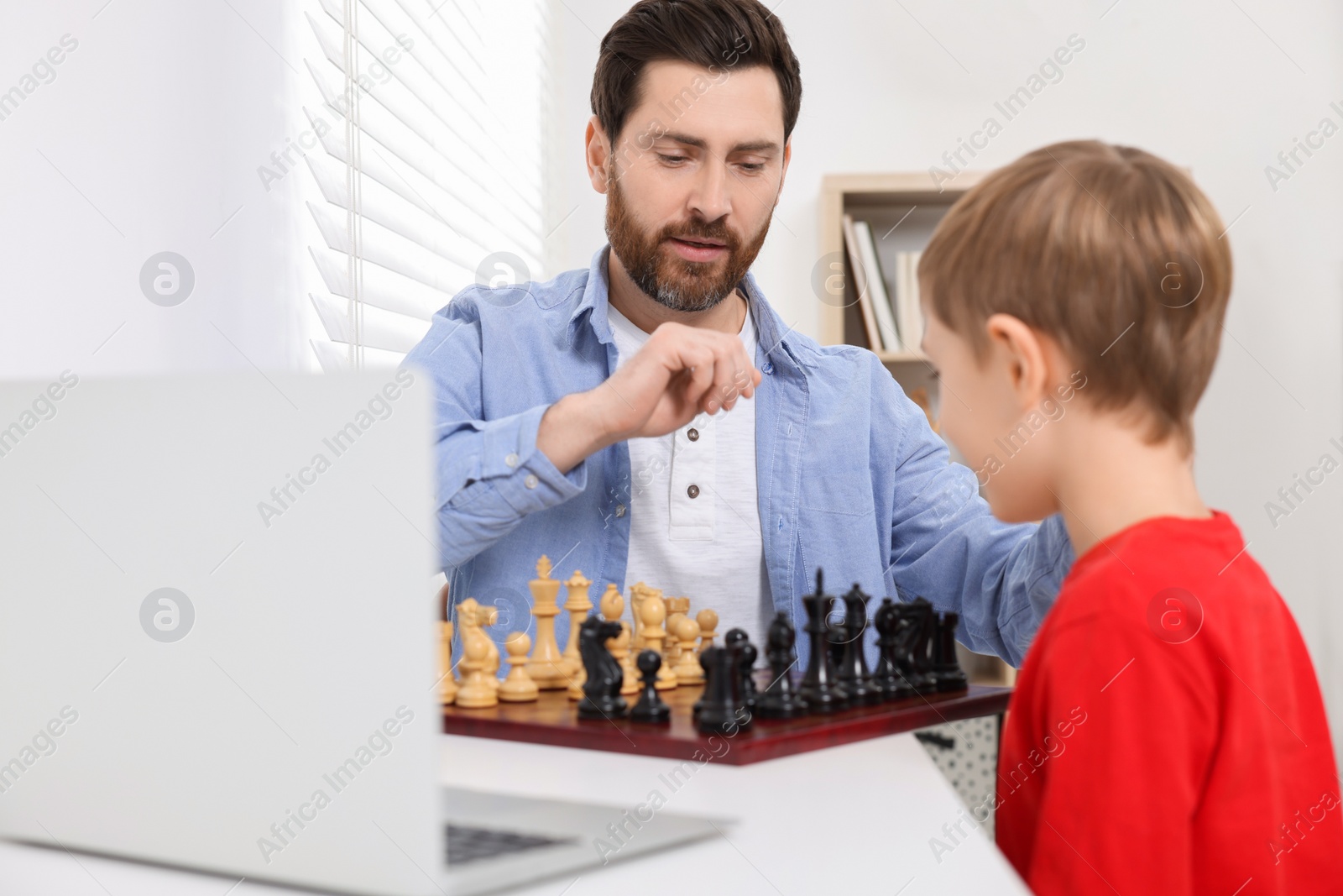 Photo of Father and son playing chess following online lesson in room