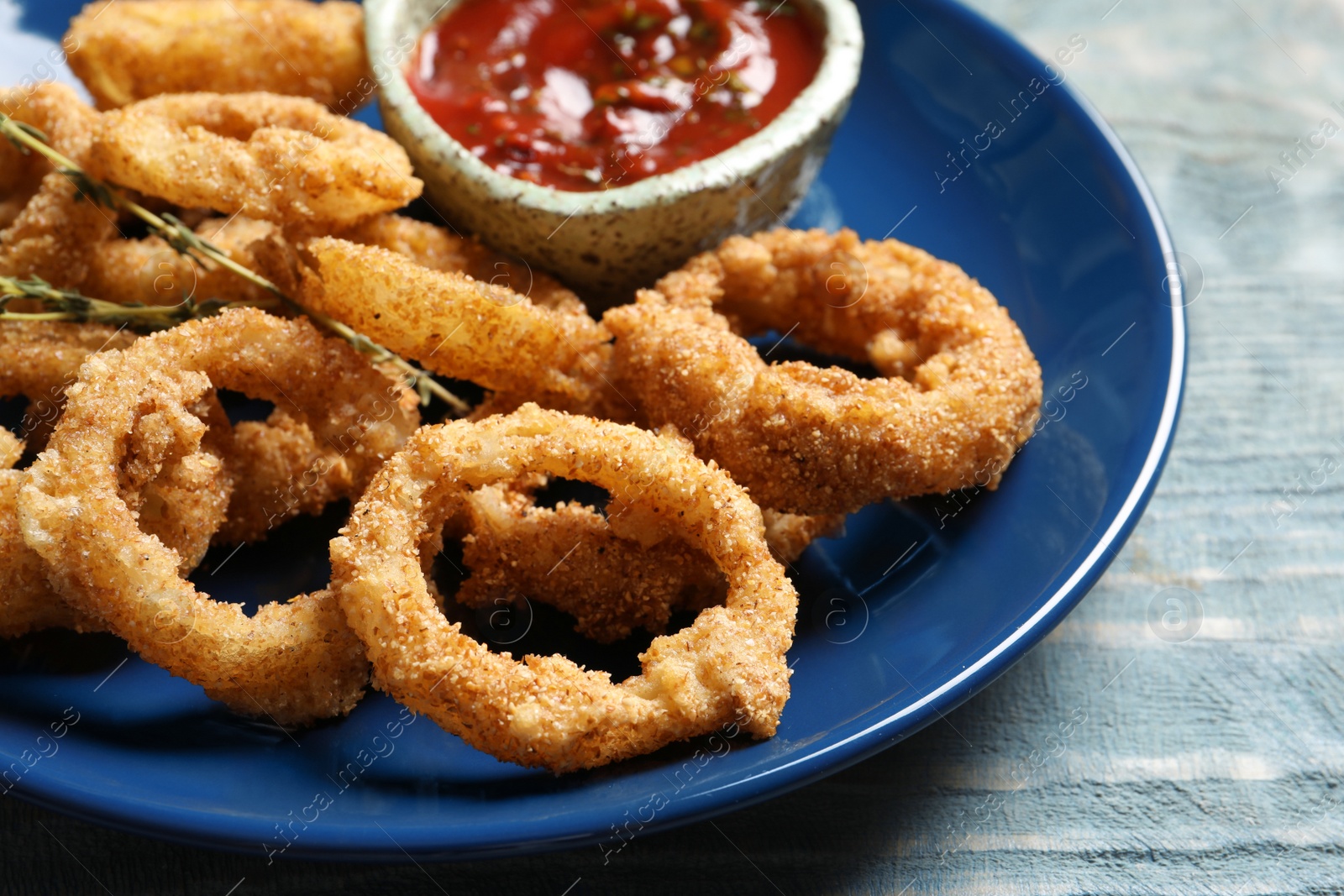 Photo of Plate with homemade crunchy fried onion rings and tomato sauce on wooden background, closeup