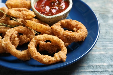 Plate with homemade crunchy fried onion rings and tomato sauce on wooden background, closeup