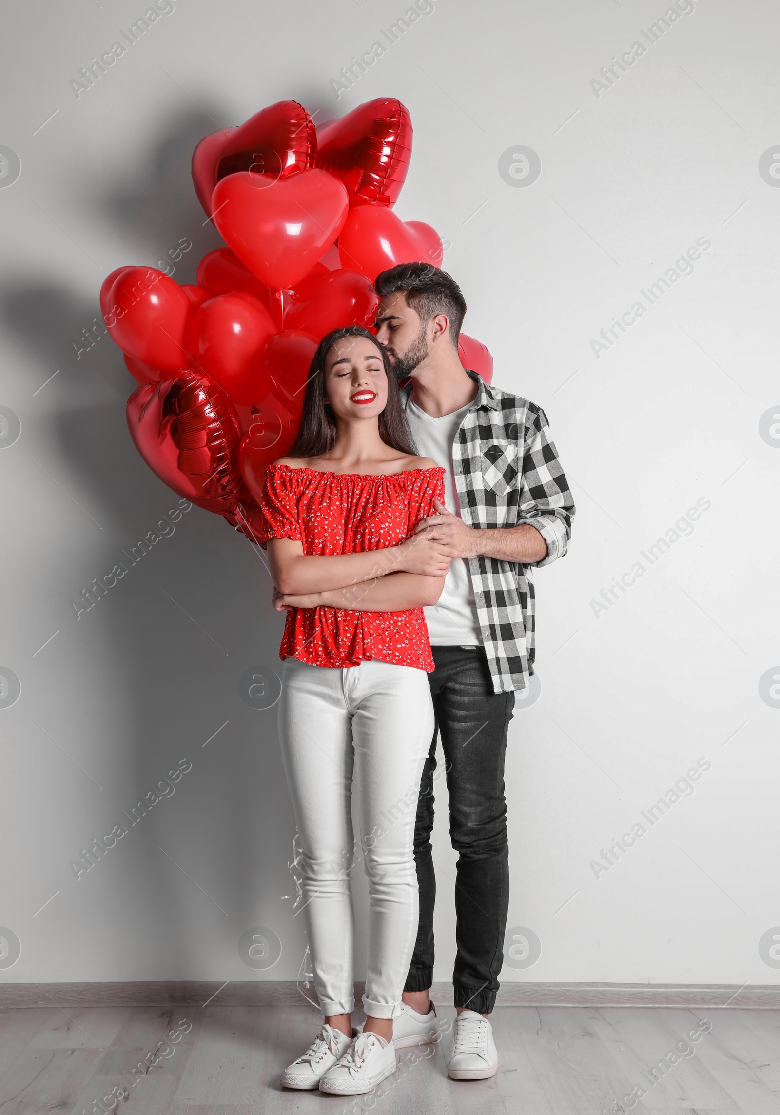 Photo of Happy young couple with heart shaped balloons near light wall. Valentine's day celebration