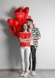 Photo of Happy young couple with heart shaped balloons near light wall. Valentine's day celebration