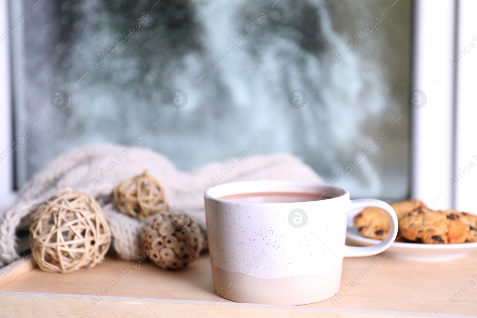 Photo of Cup of aromatic cacao on wooden tray near window, closeup