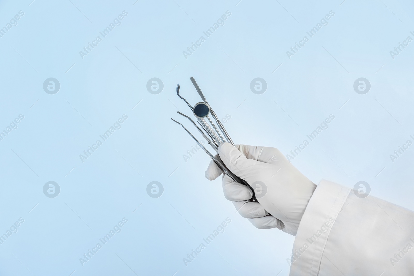 Photo of Dentist holding professional tools on light background, closeup. Space for text