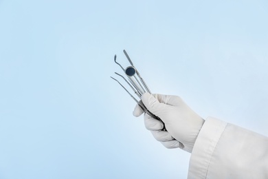 Photo of Dentist holding professional tools on light background, closeup. Space for text